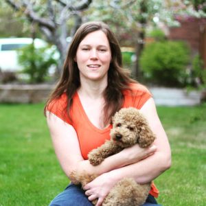 A woman holding a poodle puppy outside